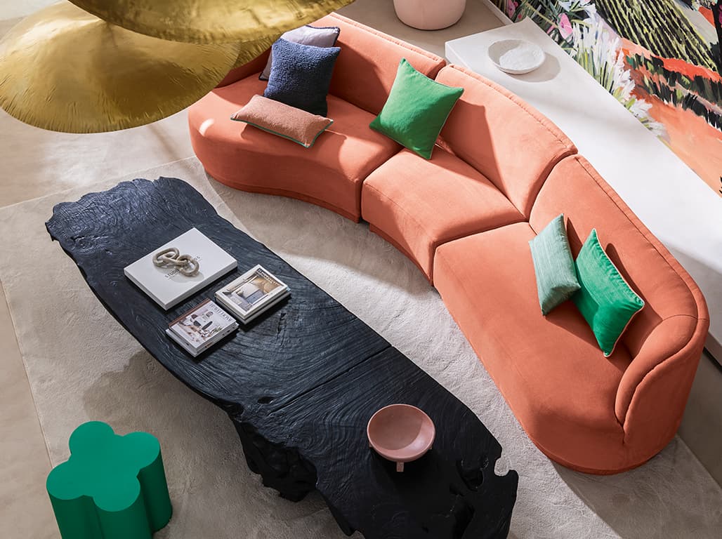 Das Bild zeigt ein Pfirsichfarbenes Sofa, fotografiert von schräg oben. Im Fokus steht ein blauer Wohnzimmertisch aus Naturholz und das mit Kissen dekorierte Sofa, dessen Farben sich in anderen Objekten im Raum wiederfinden.