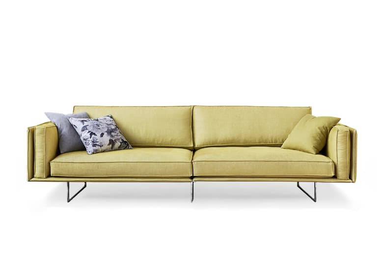 Freisteller eines gelben Sofas mit mehreren Deko-Kissen. Es besteh aus zwei Sitzflächen und die Füße sind schmale Kufen.