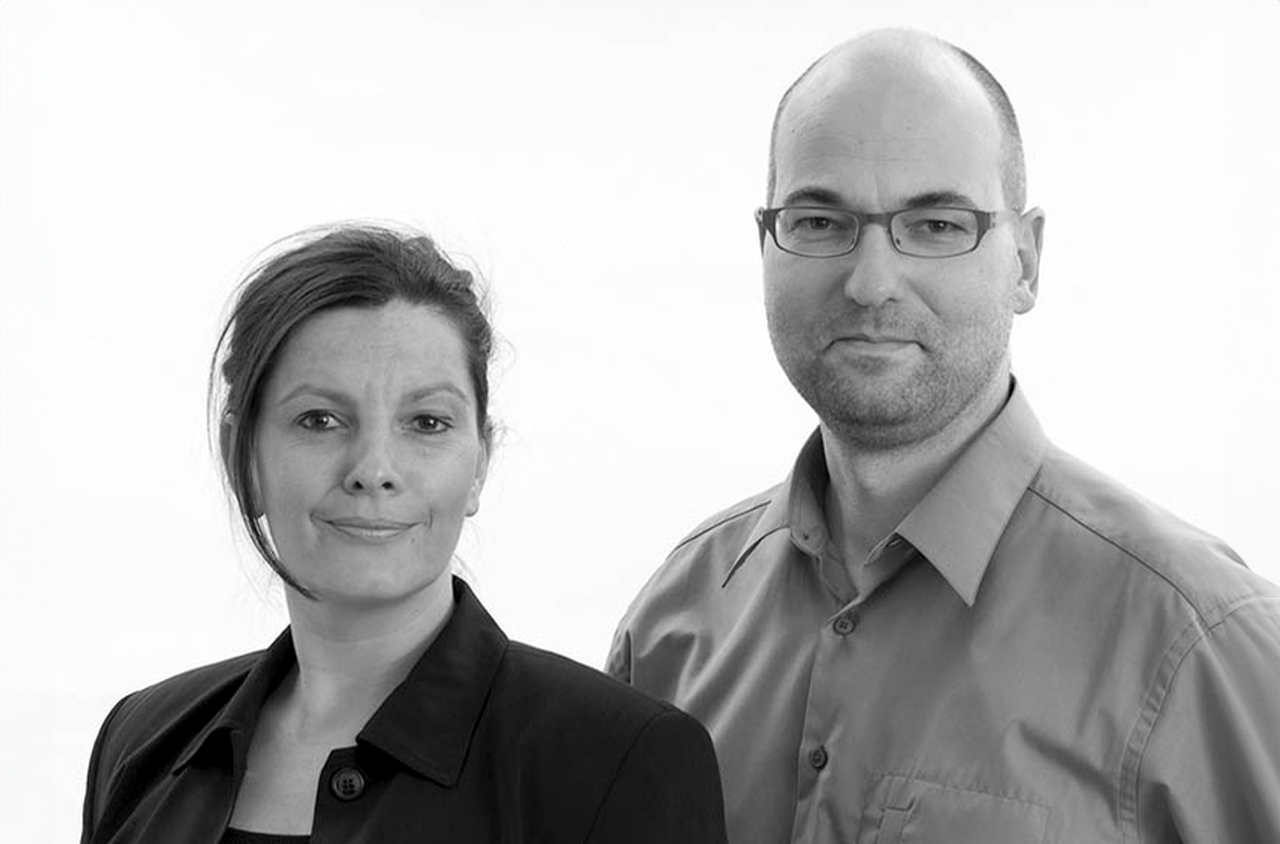 Schwarz-Weiß Portraitbild von einer Frau und eine Mann, die freundlich in die Kamera schauen. 