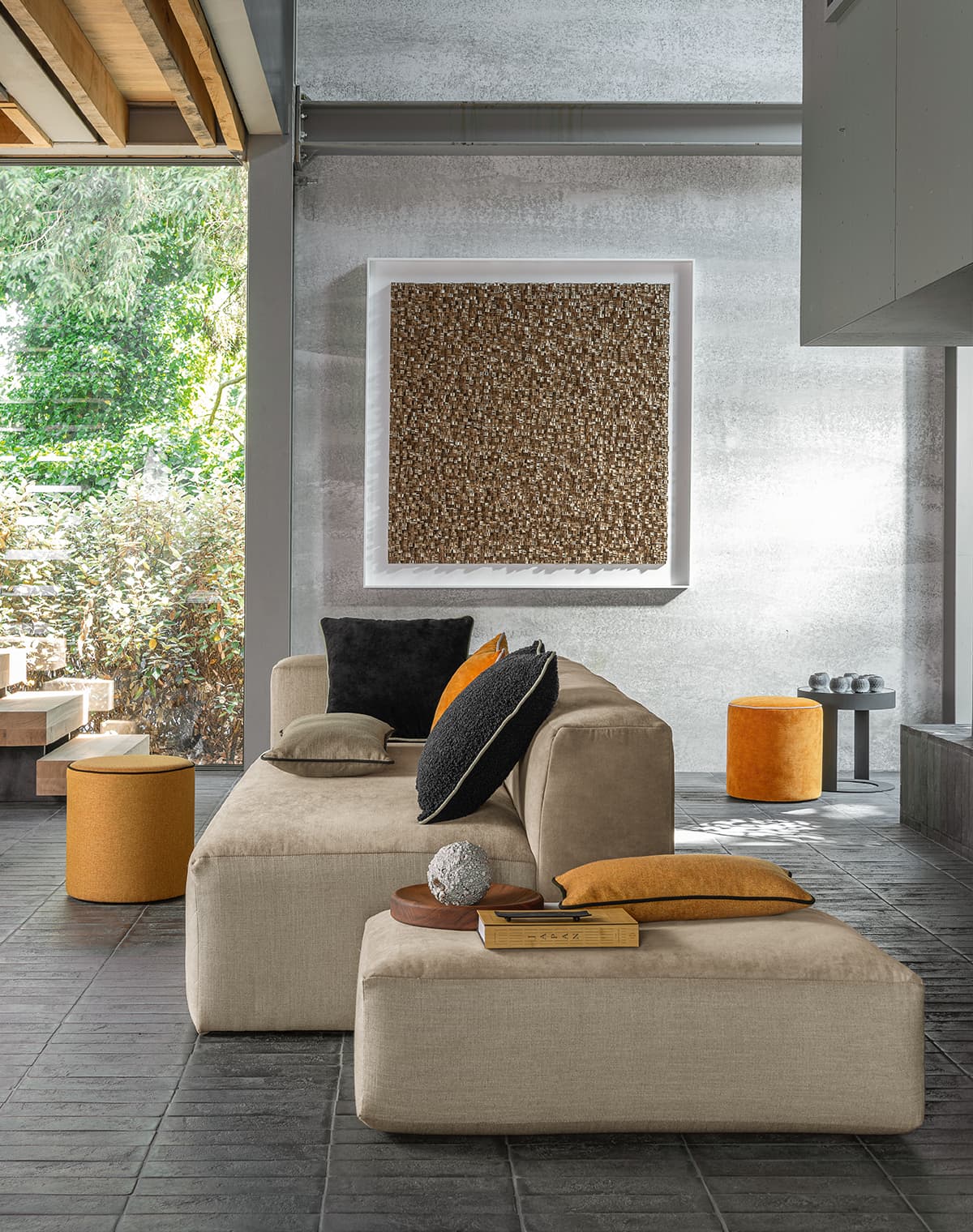 Das Bild zeigt ein beiges Sofa im Wohnzimmer. Der großzügige Bildausschnitt zeigt viel vom Raum. Orangefarbene Kissen auf der Couch harmonieren mit den orangefarbenen Poufs im Zimmer und schaffen eine einladende Atmosphäre.