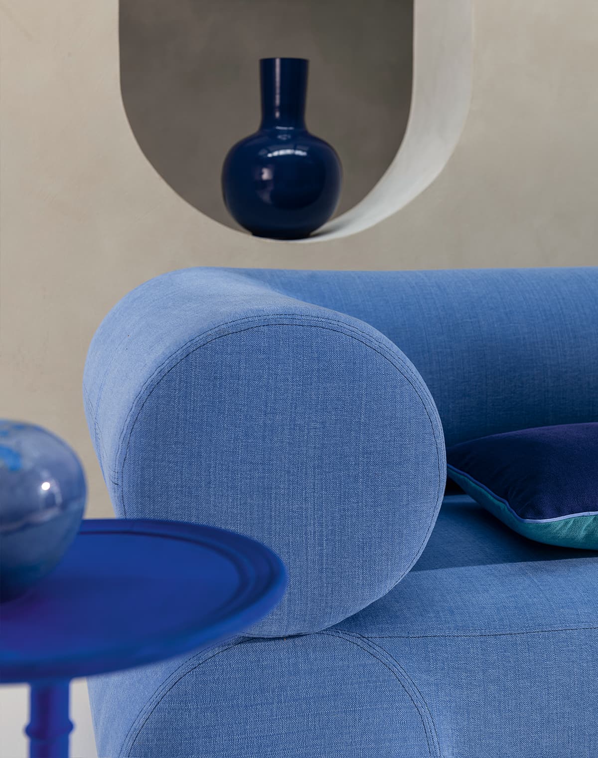 EIn blaues Sofa, ein blaues Kissen, eine blaue Vase und ein blauer Beistelltisch mit blauer Deko.