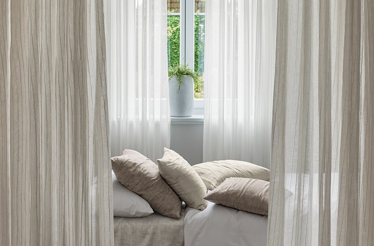 Weiße und beige Gardinen und ein Bett mit Kissen in den gleichen Farben