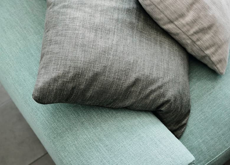 Eine Nahaufnahme von einem türkisen Sofa, zwei gräuliche Kissen liegen oben drauf.