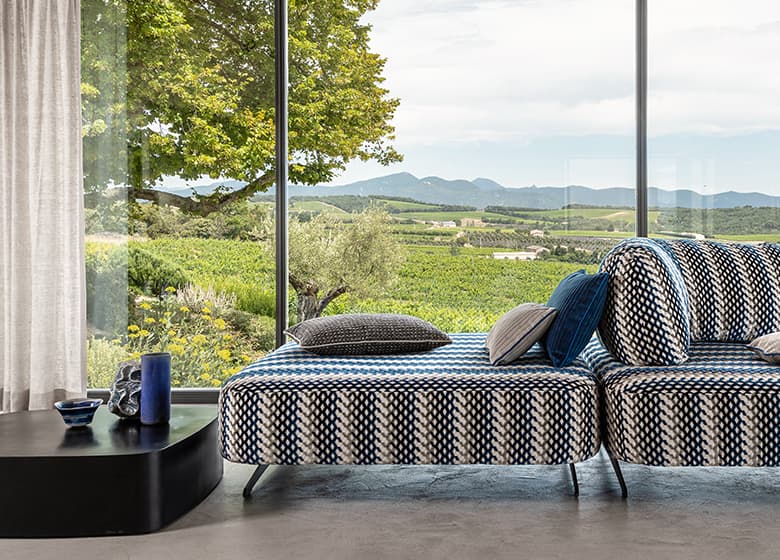 Blau-weiß gemustertes Sofa mit Kissen in grau und weiß vor einer Fensterfront.