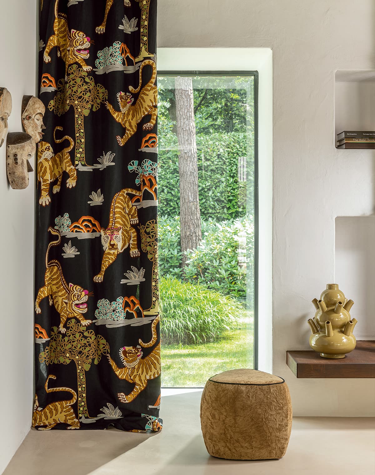 Schwarzer Vorhang mit Tiger-Print und ein brauner Pouf vor einem Fenster