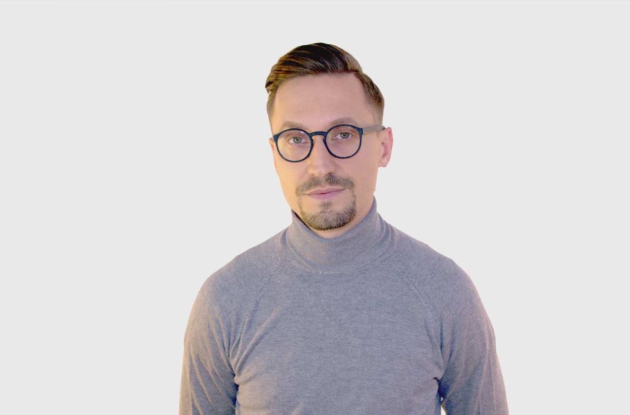 Portraitfoto von einem Mann im grauen Rollkragen Pullover und runder Brille.