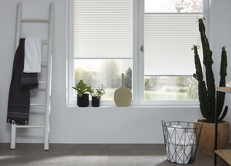 Badezimmer ausgestattet mit weißen gemusterten Plissees und Pflanzendeko auf der Fensterbank