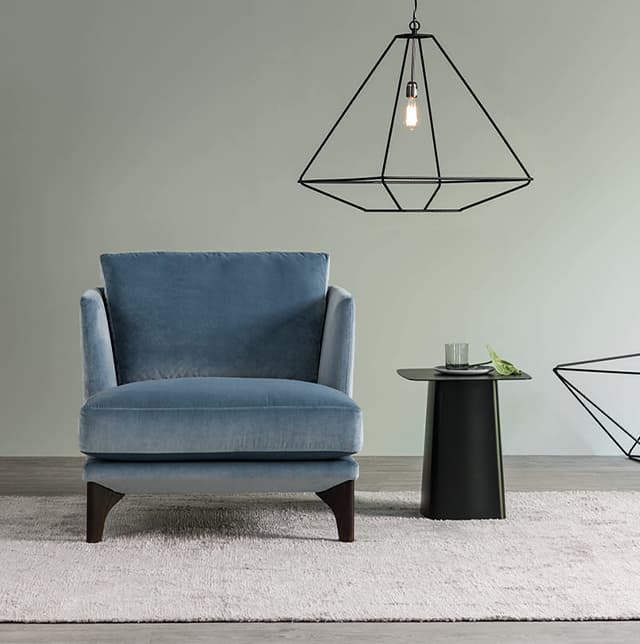 Sessel Polo Living in blau auf einem beigen Teppich, daneben steht ein schwarzer Tisch und darüber ist eine schwarze Lampe