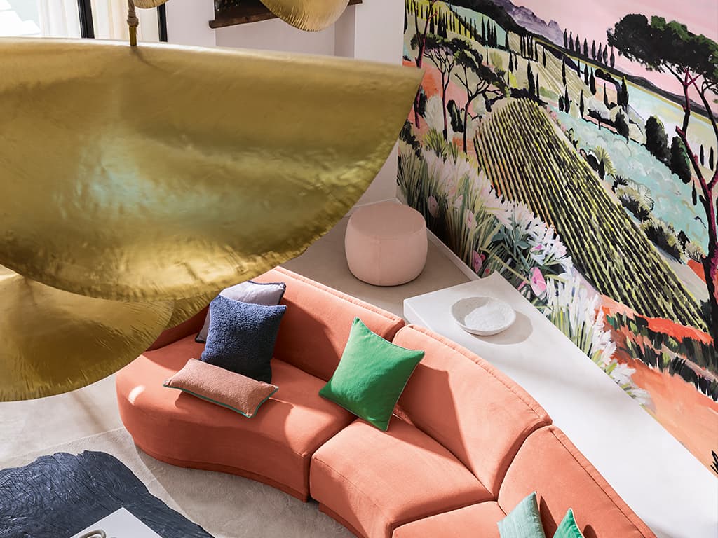 Das Bild zeigt ein Pfirsichfarbenes Sofa, fotografiert von schräg oben. Im Fokus steht ein blauer Wohnzimmertisch aus Naturholz und das mit Kissen dekorierte Sofa, dessen Farben sich in anderen Objekten im Raum wiederfinden.