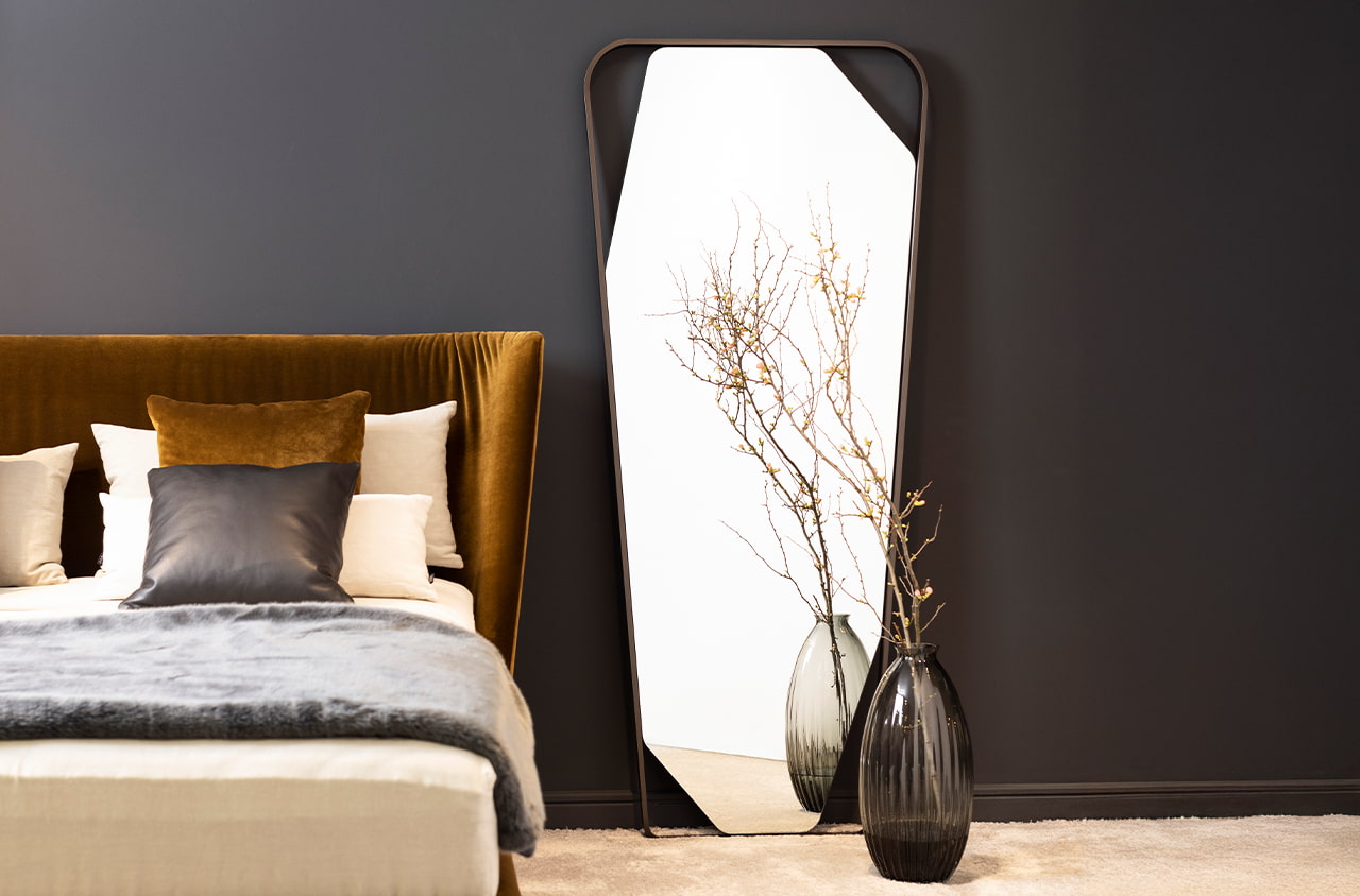 Schlafzimmer mit orangenem Bett und einem schwarzen Standspiegel mit Metallrahmen