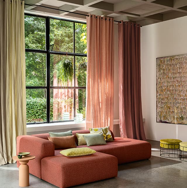 Orangenes Sofa und Vorhänge am Fenster in rot, orange, grün und gelb.