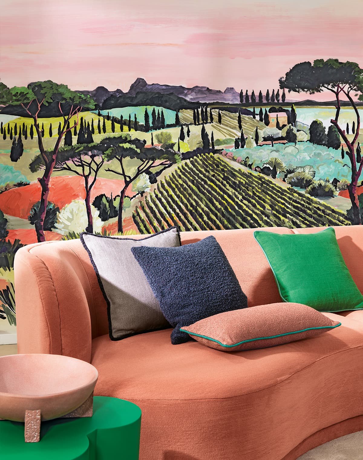 Das Bild zeigt ein koralfarbenes Sofa vor einer bunten Tapete, die dem Raum Lebendigkeit verleiht. Die unterschiedlich farbigen Kissen auf dem Sofa spiegeln die Farben der Tapete wieder.