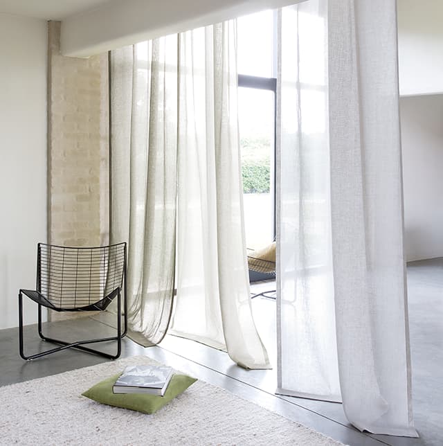 Zwei weiße transparente Vorhänge und ein Stuhl vor einem Fenster.