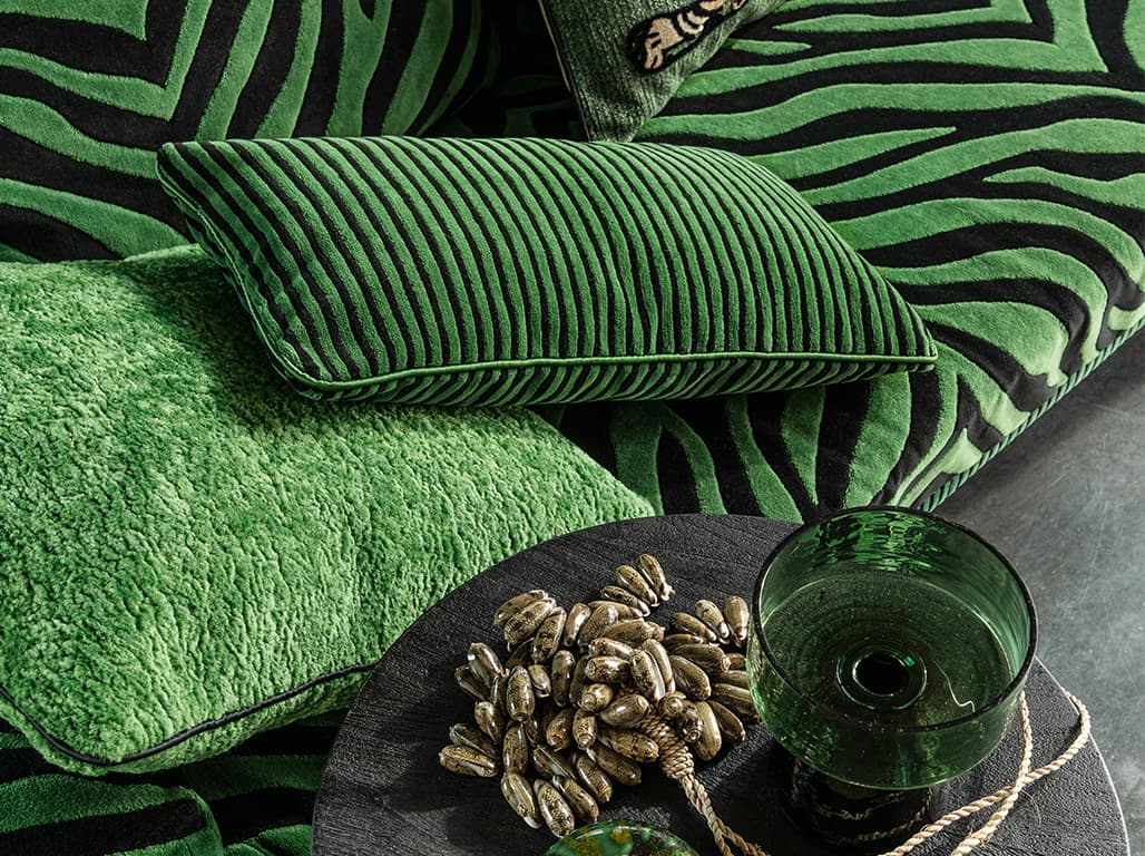 Ein grünes und ein schwarz-grün gestreiftes Kissen auf einer schwarz-grün gestreiften Couch.