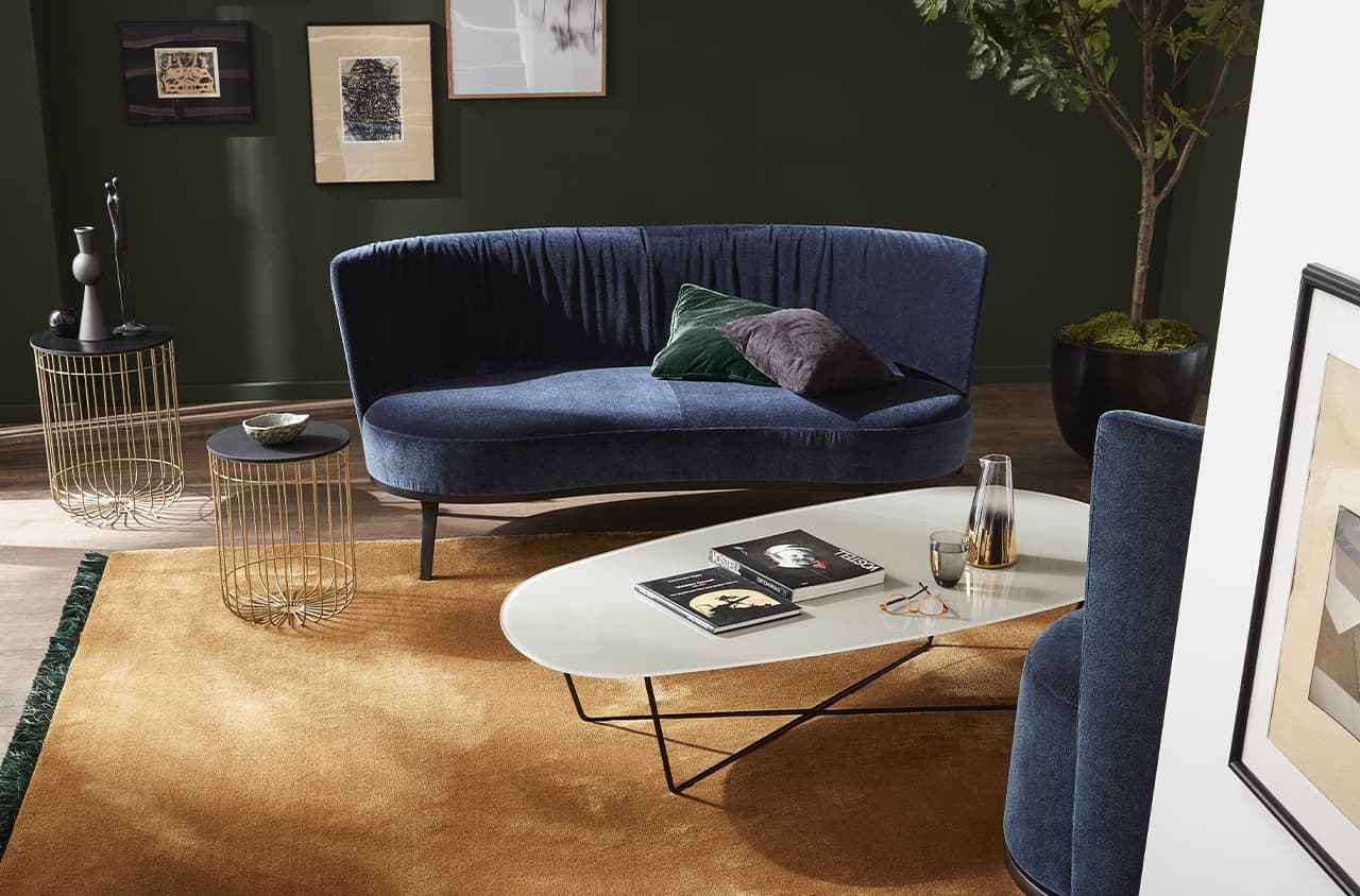Blaues Samtsofa in einem warmen dunklen Raum mit grünen Wänden und einem braunen Teppich