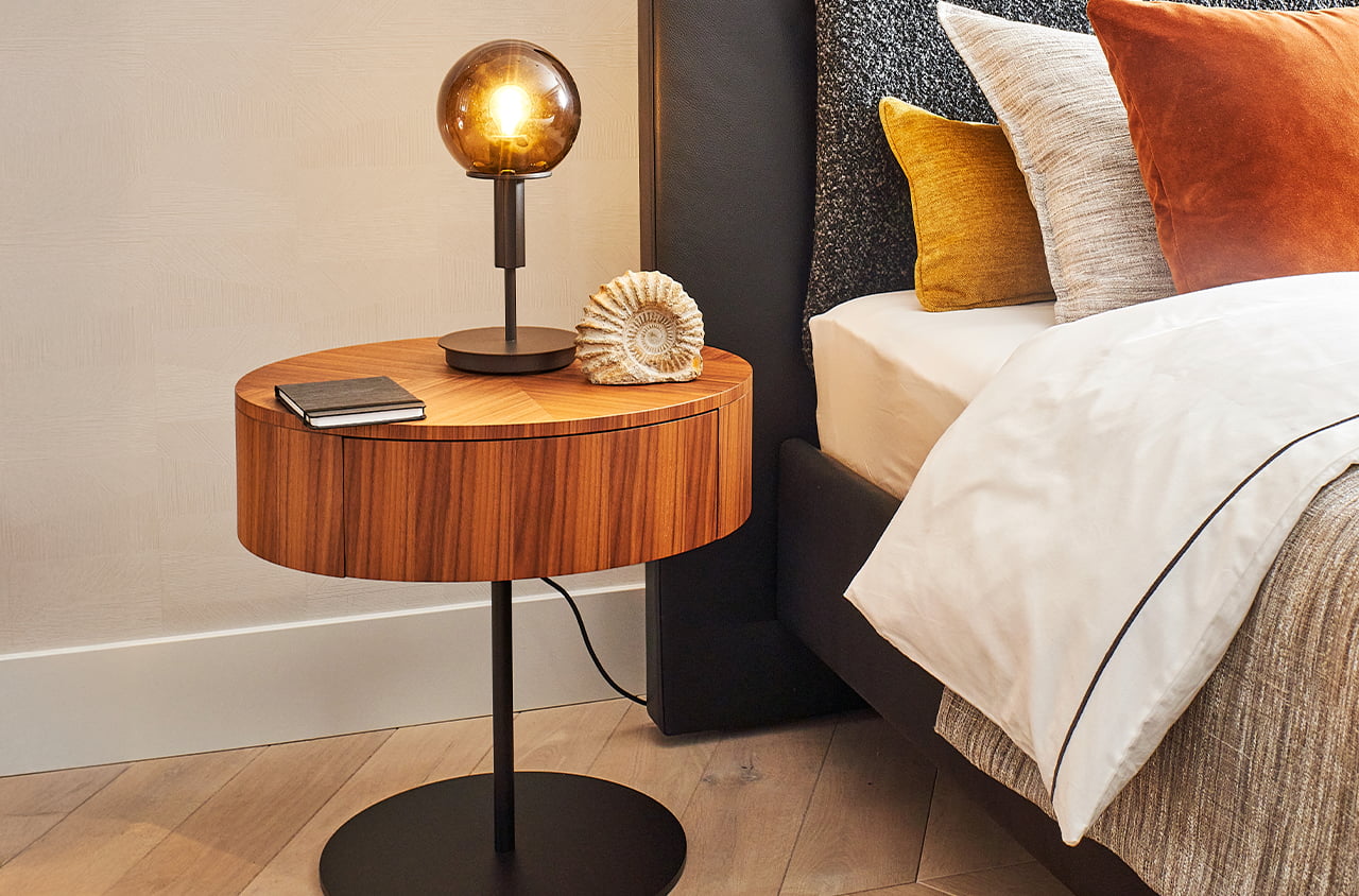 Nachttisch Kelly Grand neben einem Bett, darauf eine leuchtende Lampe und eine Muschel