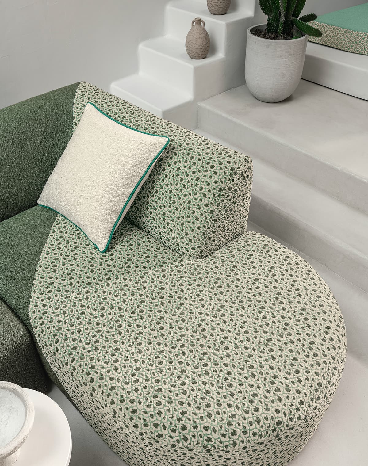 Das Bild zeigt ein grün-weißes Sofa mit Kissen vor designvollen Treppenstufen. Der Raum ist in Weiß gehalten, während eine grüne Pflanze harmonisch zum Sofa und zur Farbgestaltung des Raumes passt.